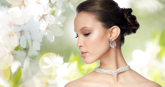 schoonheid, sieraden, accessoires, mensen en luxe concept - close-up van mooie Aziatische vrouw gezicht met oorbel over natuurlijke lente kersenbloesem achtergrond