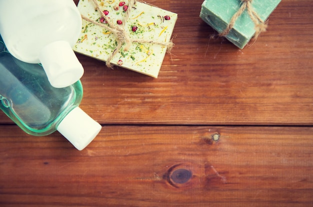 schoonheid, spa, lichaamsverzorging, bad en natuurlijke cosmetica concept - close-up van handgemaakte zeepstaven en lotionflessen op houten tafel