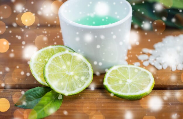 schoonheid, spa, lichaamsverzorging, natuurlijke cosmetica en wellness-concept - citrus bodylotion in kopje en zeezout met limoenen op houten tafel over lichten en sneeuw