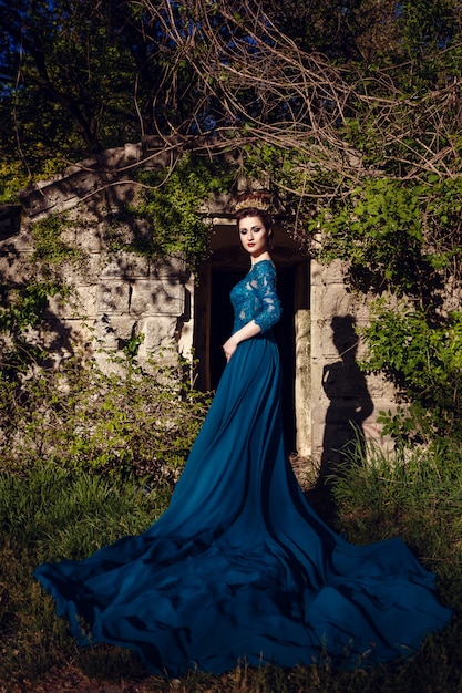 Schoonheid vrouw in groene luxe dure jurk en in de kroon op de natuur. Mooi model meisje in een groene trouwjurk. Vrouwelijk portret in het park. Vrouw met kapsel. Schattige dame buitenshuis