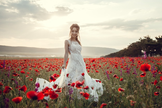 Schoonheid vrouw op papaver veld in witte jurk. Mooie bruid in Boho-stijl bij zonsondergang in een veld met rode papavers