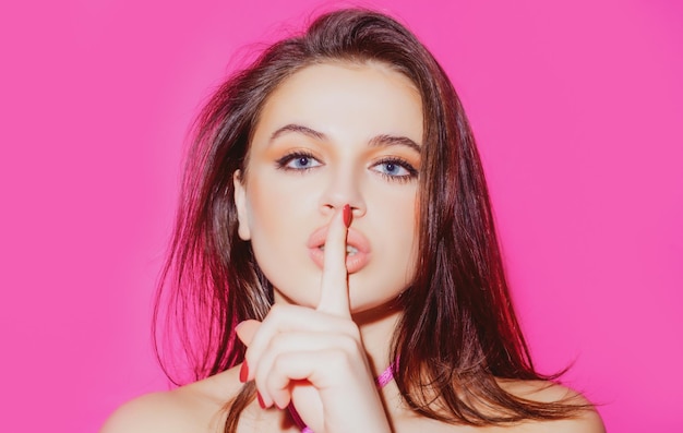 Schoonheid vrouw portret van vrij mysterieus meisje stilte shh teken met wijsvinger op lippen op roze background