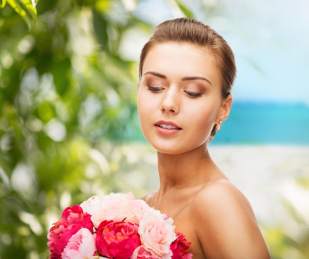 schoonheids- en sieradenconcept - vrouw die oorbellen draagt en bloemen vasthoudt