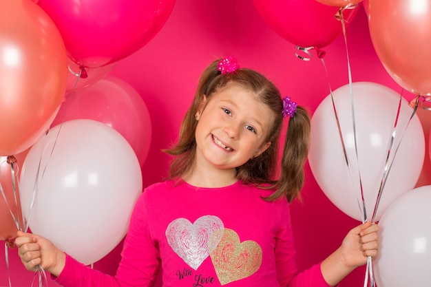 Schoonheidsmeisje die met kleurrijke luchtballons over roze achtergrond glimlachen.