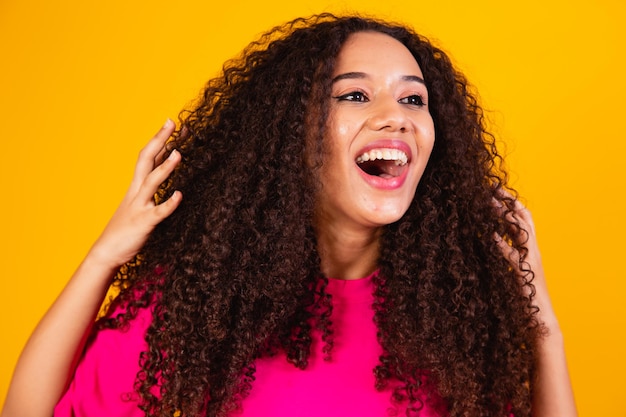 Schoonheidsportret van Afrikaanse Amerikaanse vrouw met afrokapsel en glamourmake-up. Braziliaanse vrouw. Gemengd ras. Gekruld haar. Haarstijl. gele achtergrond