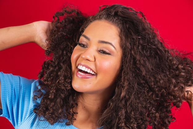 Schoonheidsportret van Afrikaanse Amerikaanse vrouw met afrokapsel en glamourmake-up. Braziliaanse vrouw. Gemengd ras. Gekruld haar. Haarstijl. Rode achtergrond.