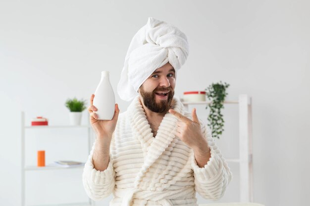 Schoonheidsportret van een knappe, mooie kerel in een handdoek en badjas die een tube bodycrèmelotion in de hand houdt. spa, lichaam en huidverzorging voor man concept.