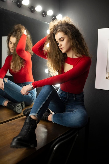 Foto schoonheidsportret van een sensuele jonge vrouw met krullend haar zittend op houten tafel poseren in de buurt van spiegel