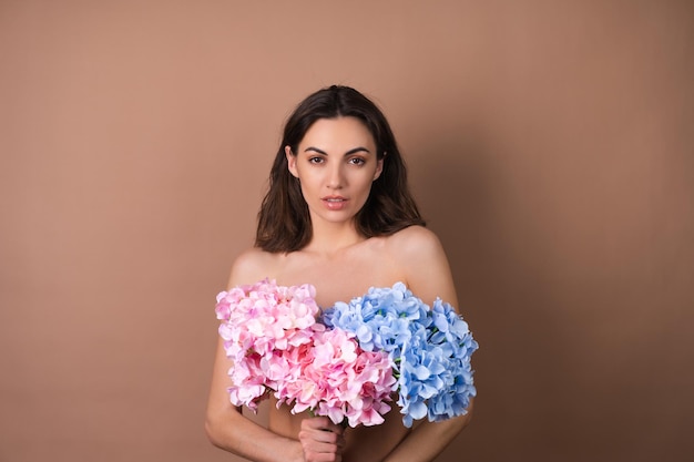 Schoonheidsportret van een topless vrouw met een perfecte huid en natuurlijke make-up op een beige achtergrond met een boeket van kleurrijke bloemen