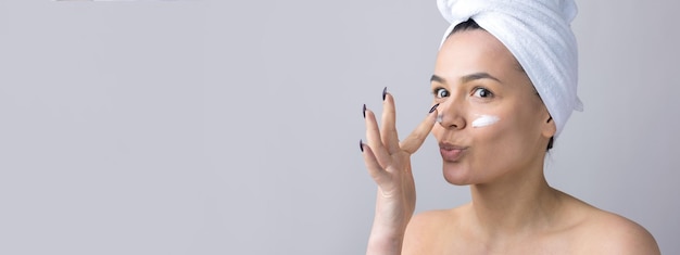 Schoonheidsportret van een vrouw in een witte handdoek op het hoofd brengt crème aan op het gezicht Huidverzorging reiniging eco-organische cosmetische spa relax concept