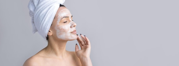 Schoonheidsportret van een vrouw in een witte handdoek op het hoofd brengt crème aan op het gezicht Huidverzorging reiniging eco-organische cosmetische spa relax concept