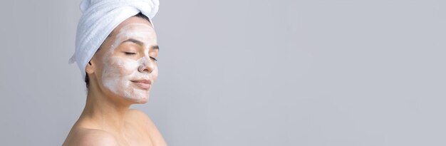 Schoonheidsportret van een vrouw in een witte handdoek op het hoofd brengt crème aan op het gezicht Huidverzorging reiniging eco-organische cosmetische spa relax concept