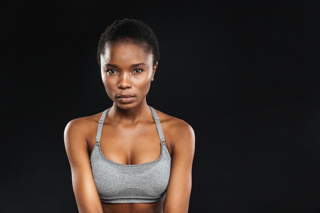 Schoonheidsportret van fitnessvrouw met perfecte huid die naar voorzijde kijkt die op een zwarte muur wordt geïsoleerd