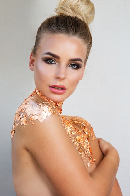 Schoonheidsportret van glamoureuze blondevrouw met lichte make-up en gouden folie op haar schouders