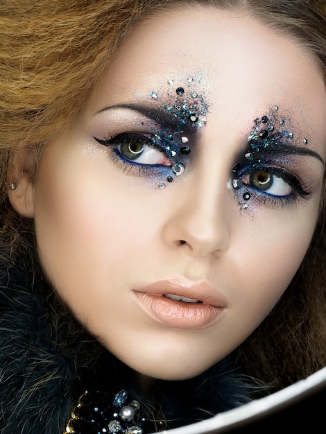 Schoonheidsportret van jonge vrouw met moderne maniermake-up met strass steentjes. Carnaval of partijmake-up