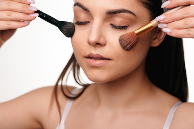 Schoonheidsportret van kaukasische jonge donkerbruine vrouw die schoonheidsmiddelen met make-upborstel toepast
