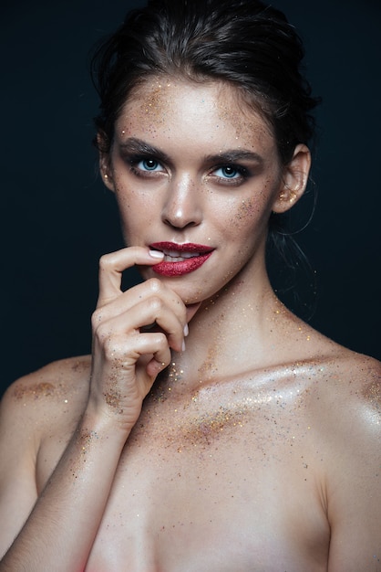 Foto schoonheidsportret van leuke speelse jonge vrouw met heldere glanzende make-up die haar lippen over zwart oppervlak aanraakt