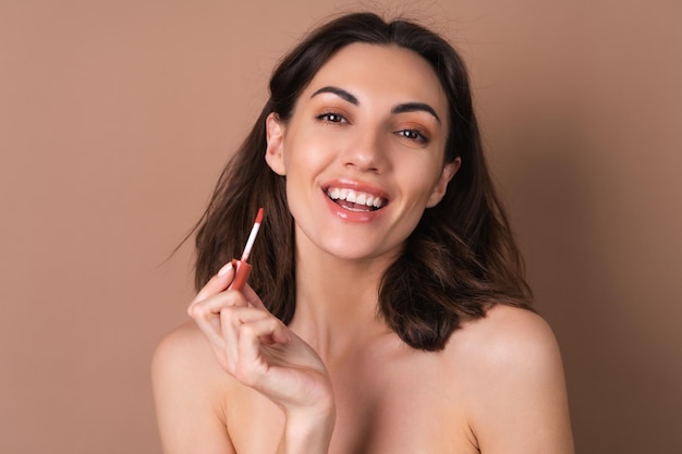 Foto schoonheidsportret van topless vrouw met perfecte huid en natuurlijke make-up op beige achtergrond met bruine chocoladeglans lippenstift