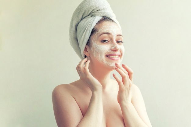 Schoonheidsportret van vrouw in handdoek op hoofd met wit voedend masker of room op gezicht, witte geïsoleerde achtergrond. Huidverzorging reiniging eco organische cosmetische spa relax concept