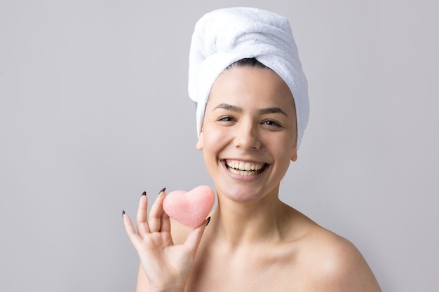 Schoonheidsportret van vrouw in witte handdoek op hoofd met een spons voor een lichaam met het oog op een roze hart