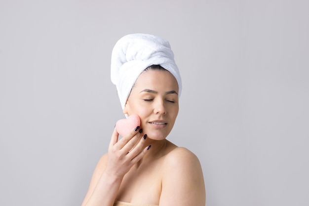 Schoonheidsportret van vrouw in witte handdoek op hoofd met een spons voor een lichaam met het oog op een roze hart