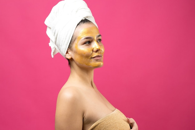 Schoonheidsportret van vrouw in witte handdoek op hoofd met gouden voedend masker op gezicht. Huidverzorging reiniging eco biologische cosmetische spa ontspannen concept.