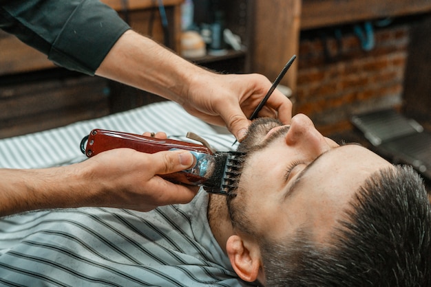 Schoonheidssalon voor mannen. Een baard scheren in een herenkapper. Kapper snijdt zijn baard met een scheermes en een tondeuse. close up Brute kapsels. Kapper apparatuur. Selectieve aandacht.