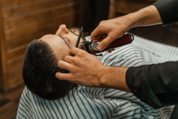 Schoonheidssalon voor mannen. Een baard scheren in een herenkapper. Kapper snijdt zijn baard met een scheermes en een tondeuse. close up Brute kapsels. Kapper apparatuur. Selectieve aandacht.