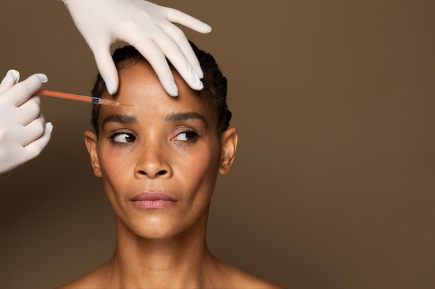 Schoonheidsspecialist boctor die botox-injectie maakt in de interbrow-zone tot zwarte vrouw van middelbare leeftijd bruin