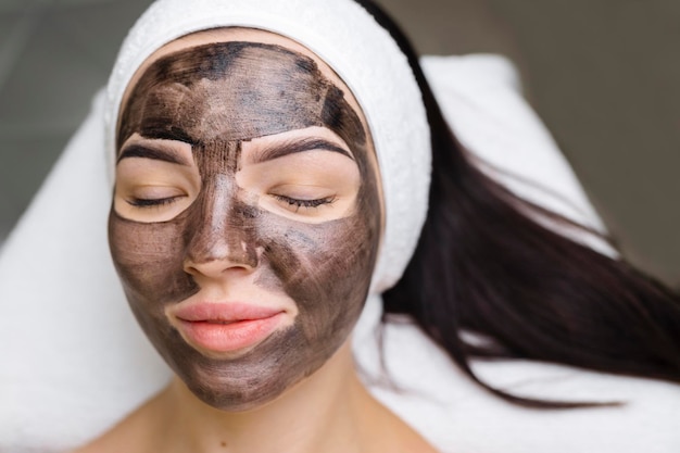 Schoonheidsspecialist die een zwart masker toepast op het gezicht van een mooie vrouw met zwarte handschoenen, een prachtige vrouw in de spa met gezichtsprocedures