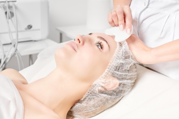 Schoonheidsspecialist die gezichtsmassage maakt met Gua Sha-steen van de gezichtshuid van de vrouw voor lymfedrainage