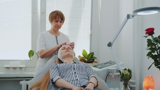 Schoonheidsspecialist die vrouw voor het maken van gezichtsreiniging in schoonheidssalon voorbereiden