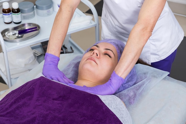 Schoonheidsspecialist die zich voorbereidt op het doen van cosmetische gezichtsbehandelingen voor de jonge vrouw.