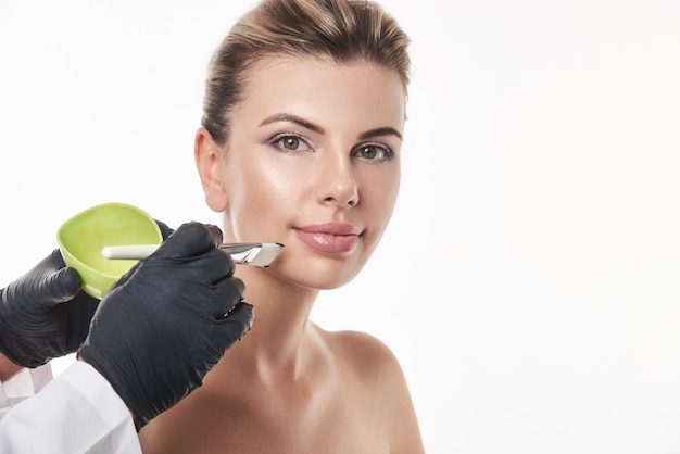 Schoonheidsspecialist handen met een groene kom met exfoliant crème of gezichtsmasker