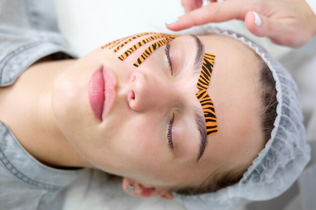 Schoonheidsspecialist maken tape gezicht procedure met behulp van tijger gekleurde tapes in schoonheidssalon