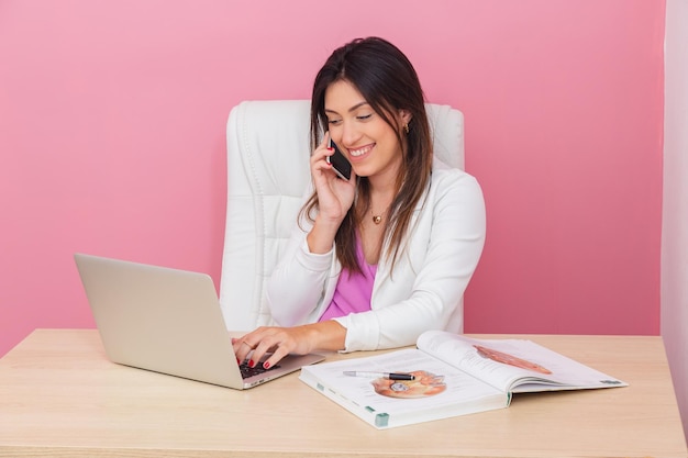 Schoonheidsspecialiste arts zakenvrouw succesvolle ondernemer glimlachend esthetische professional typen op notebook en praten op mobiele telefoon