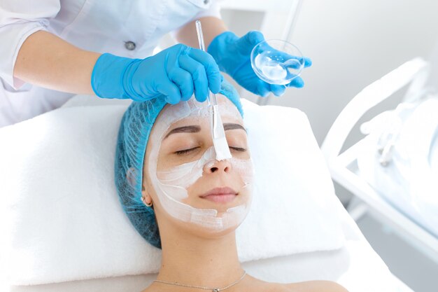 Schoonheidsspecialiste brengt een masker aan op het gezicht van een patiënt voor huidverzorging