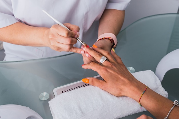 Schoonheidsspecialiste die meerkleurige nagellak met borstel uitvoert in een schoonheidssalon.