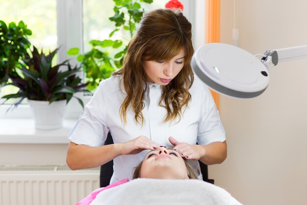 Schoonheidsspecialiste gezichtsmassage doen met vrouw in kliniek