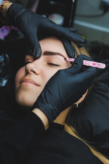 Schoonheidsspecialiste hand doen wenkbrauw permanente make-up op een aantrekkelijk vrouwelijk gezicht