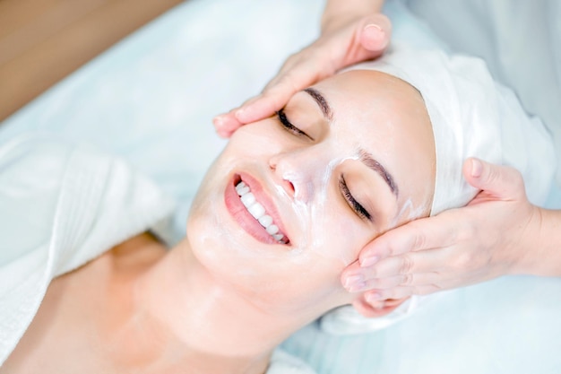 Schoonheidsspecialiste maakt gezichtsmassage met masker mooi lachend meisje op spa-procedure door gezicht