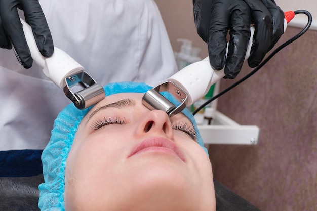 Schoonheidsspecialiste masseert het gezicht van de patiënt met laagspanningsmicrostromen