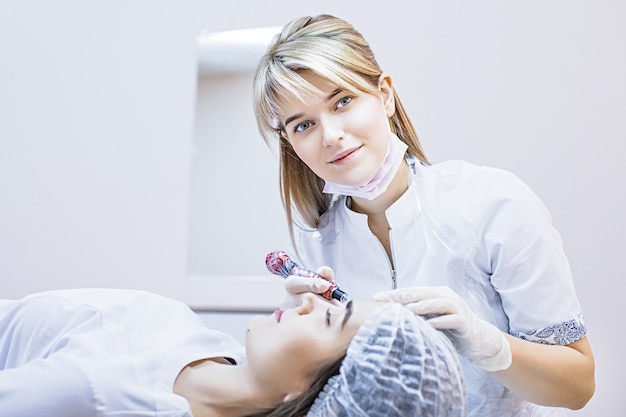 Schoonheidsspecialiste vrouw brengt permanente make-up aan op wenkbrauwen tatoeage wenkbrauwen op mooie modellen in een schoonheidssalon