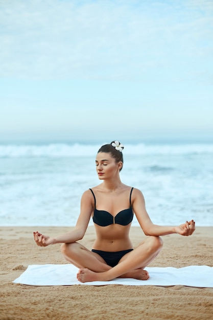 Schoonheidsvrouw beoefent yoga en mediteert in de lotuspositie op het strand. Meditatie. Actieve levensstijl. Gezond en yogaconcept. Fitness en sport