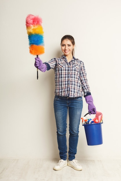 Schoonmaak diensten concept. Jonge vrouw met emmer met wasmiddelen en vodden op witte geïsoleerde achtergrond. Huishoudelijke en huishoudelijke schoonmaak