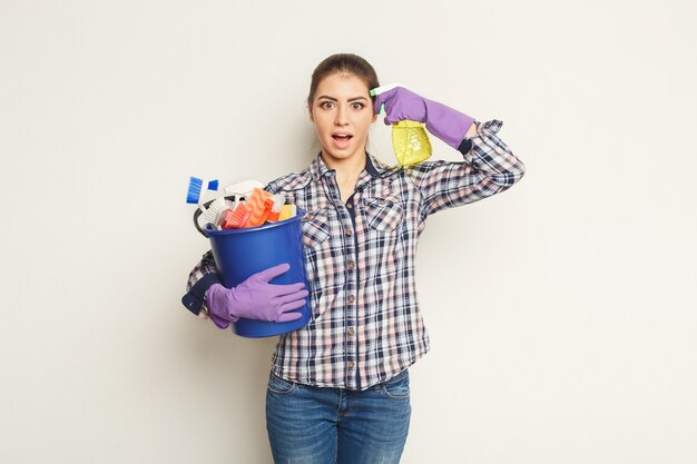 Schoonmaak diensten concept. Jonge vrouw met emmer met wasmiddelen en vodden op witte geïsoleerde achtergrond. Huishoudelijke en huishoudelijke schoonmaak