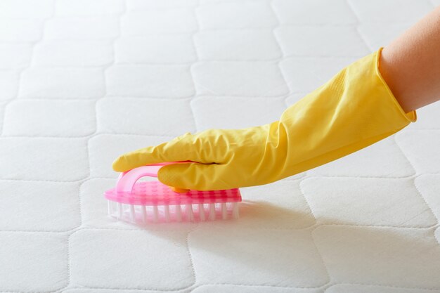 Schoonmaakbedrijf Medewerker hand reinigt oppervlak van matras op bed met borstel. Reinigen van desinfectieoppervlakken. Hand in handschoen doen Matras chemisch reinigen.
