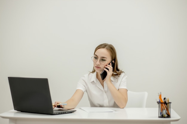 Schot gelukkig zakenvrouw zittend aan een bureau achter haar laptop en praten met iemand op haar mobiele telefoon tijdens het werken vanuit huis. thuiskantoor.