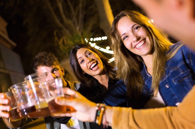 Schot van aantrekkelijke jonge vrienden die roosteren met bier in de eetmarkt op straat.