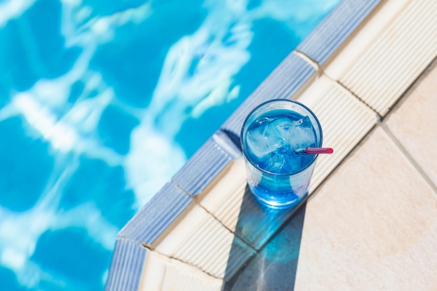 Schot van bovenaf van zomerse frisdranken Blauwe lagunecocktail met ijs bij zwembad op zonnige dag